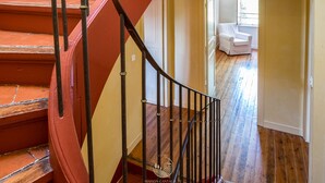 A staircase with red steps and black railings leading to a room with a white chair and wooden flooring. - La Maison Vigneronne (Trebes)