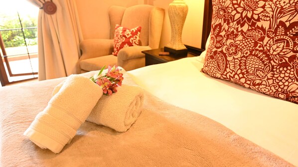 A neatly made bed with a rolled white towel and a small bouquet of flowers.