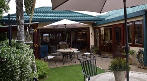 An outdoor patio area with a table and chairs, a large umbrella, and a view of the interior through glass doors.