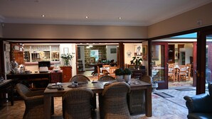 A spacious dining area with wicker chairs and a large table, leading to a kitchen and a dining room with wooden furniture. - Lamor Guest House (Middelburg)