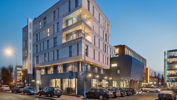 Un hotel moderno de varios pisos, con amplias ventanas y un estacionamiento con varios automóviles.