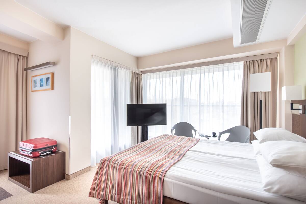 Une chambre d’hôtel avec un lit, une télévision, un bureau avec une valise rouge et une chaise.