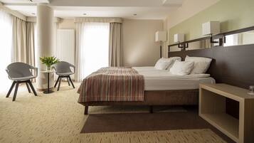 A hotel room with a bed, bedside table, lamp, chair, and a small table with a plant.