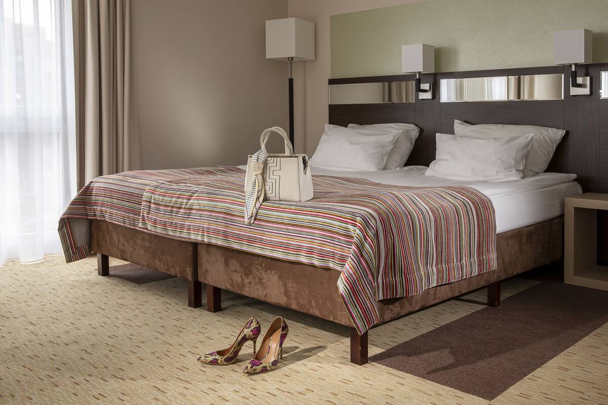 Une chambre d’hôtel avec un grand lit, une table de chevet, une lampe et un sac à main posé sur le lit.