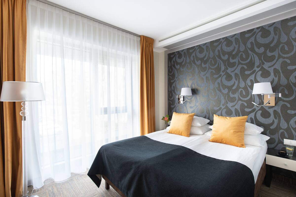 Une chambre d’hôtel avec un grand lit, deux lampes de chevet, une table de chevet et un papier peint à motifs.