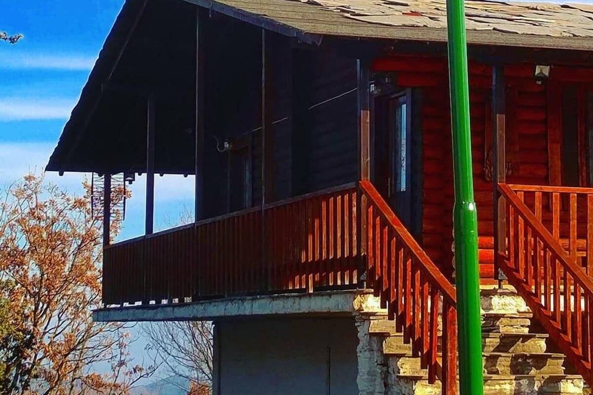 A wooden cabin with a stone staircase leading to a porch, a green pole with a spherical light, and a clear blue sky.