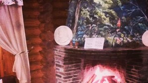 Een stenen openhaard met daarin een vlam, een decoratief muurschildering erboven en een bord op de schoorsteenmantel.