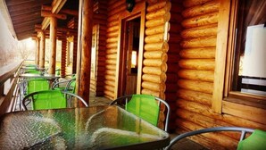 Een blokhut met een overdekte buitenruimte, inclusief metalen tafels en groene stoelen.