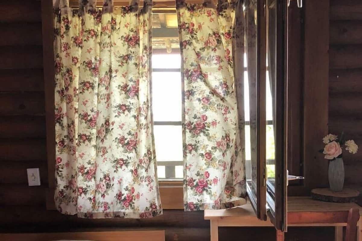 A cabin room with a bed, a wooden desk, and a window with floral curtains.