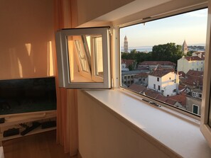 A room with a window overlooking a cityscape, including a prominent tower.