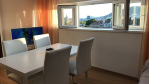 A modern room with a dining table, white chairs, a TV, and a window with a city view. - Apartments Istarska - Adults Only (Split)