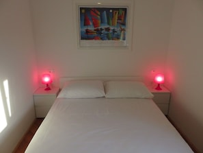 A bedroom with a bed, two bedside lamps, a nightstand, and a framed painting on the wall.