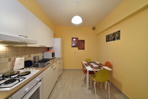 Une cuisine compacte équipée d’une cuisinière à gaz, d’un four à micro-ondes et d’un évier. On y trouve une table à manger avec des chaises et un petit tableau accroché au mur.