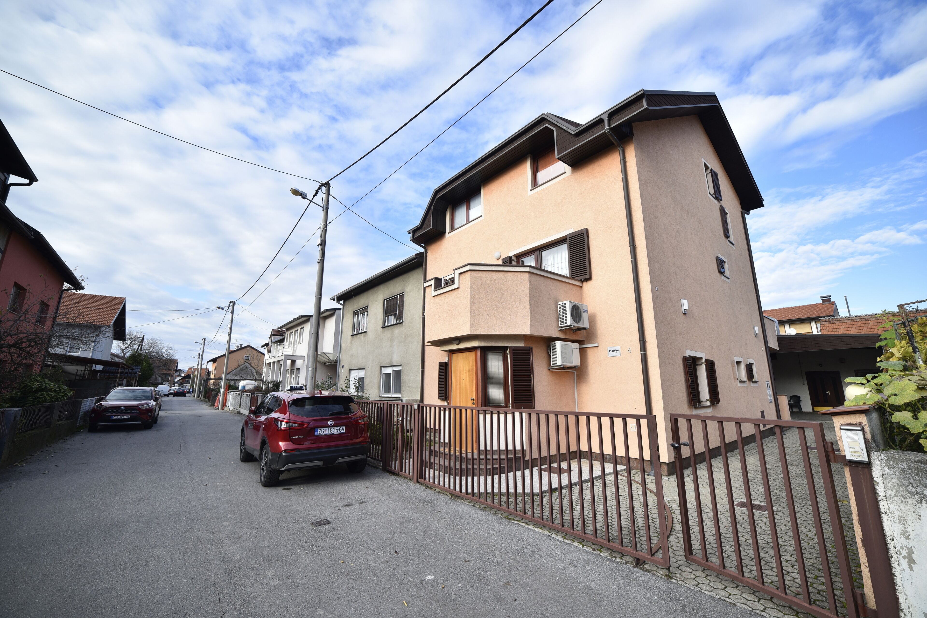 Una calle residencial con casas, un acceso con portón cerrado y coches estacionados.