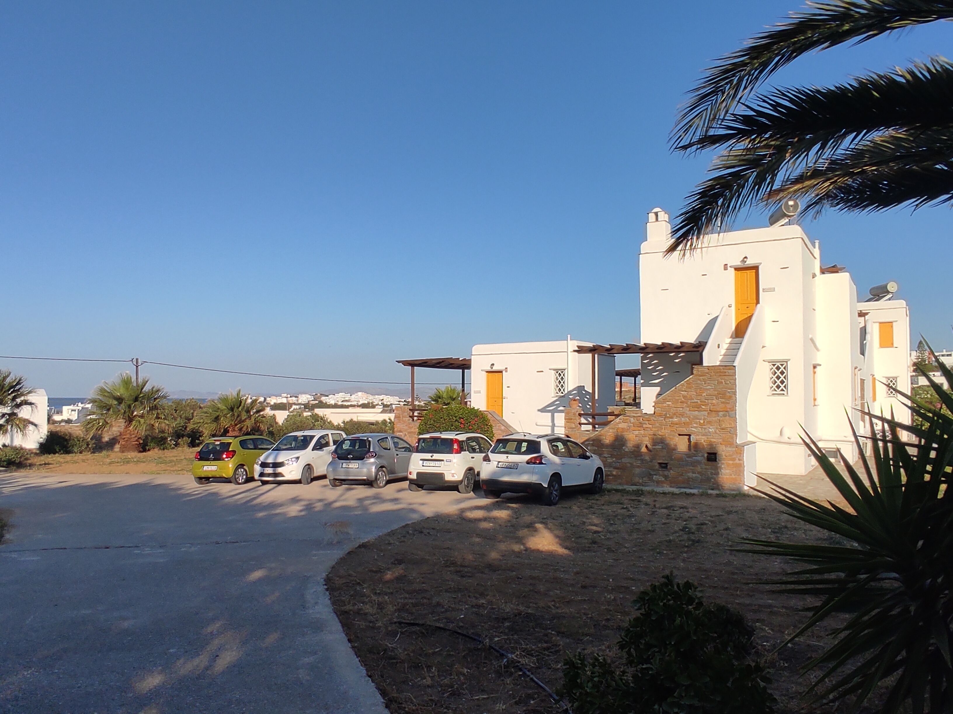 A parking area with several cars, a white building with a stone facade, and a clear blue sky.