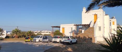 A parking area with several cars, a white building with a stone facade, and a clear blue sky.