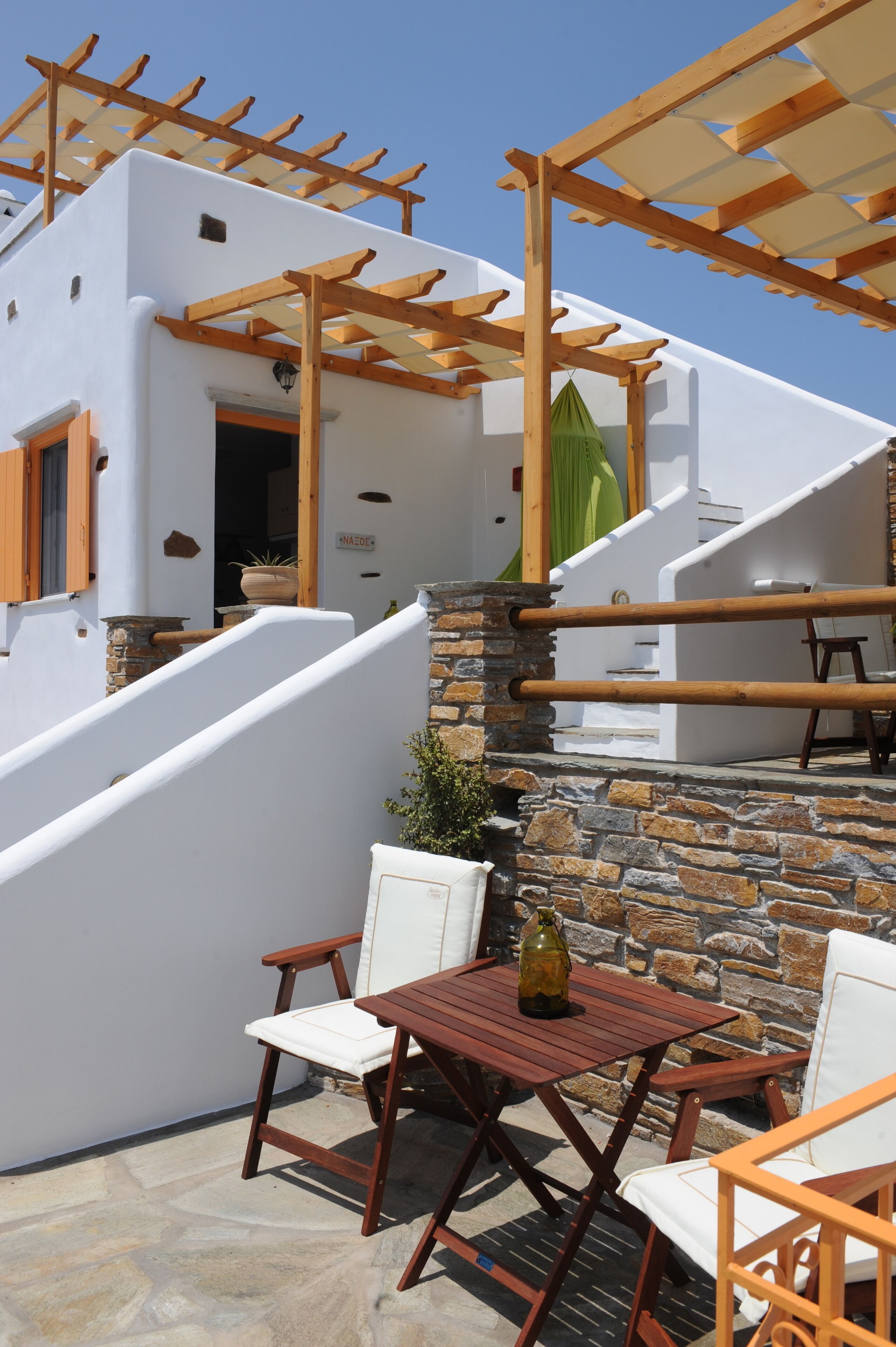 Una terraza con muro de piedra, pérgola de madera y mobiliario exterior.