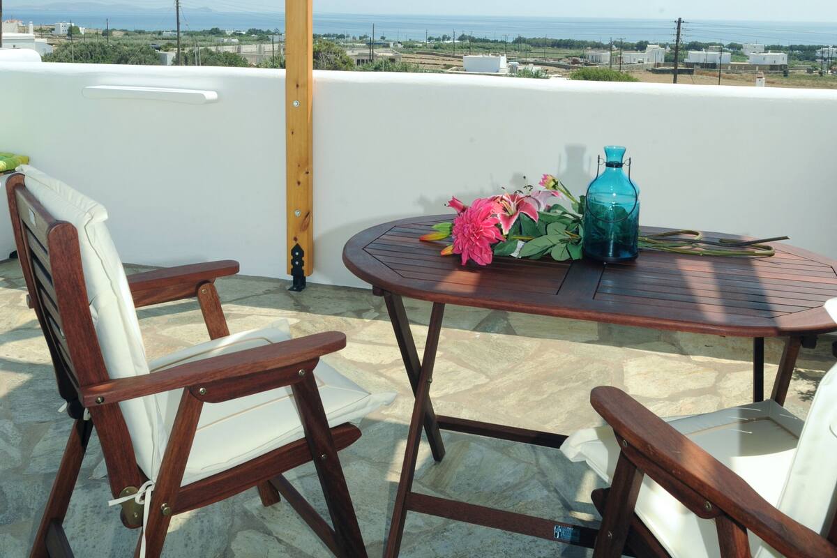 Una pérgola de madera con una mesa y sillas en una terraza en la azotea con vistas a un paisaje costero.