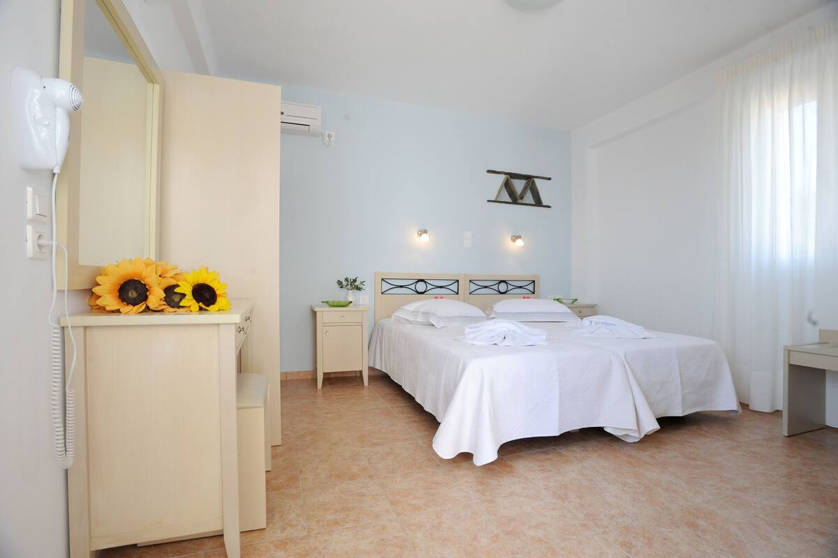 Un dormitorio con cama, mesita de noche, cómoda, espejo y lámpara fijada a la pared.