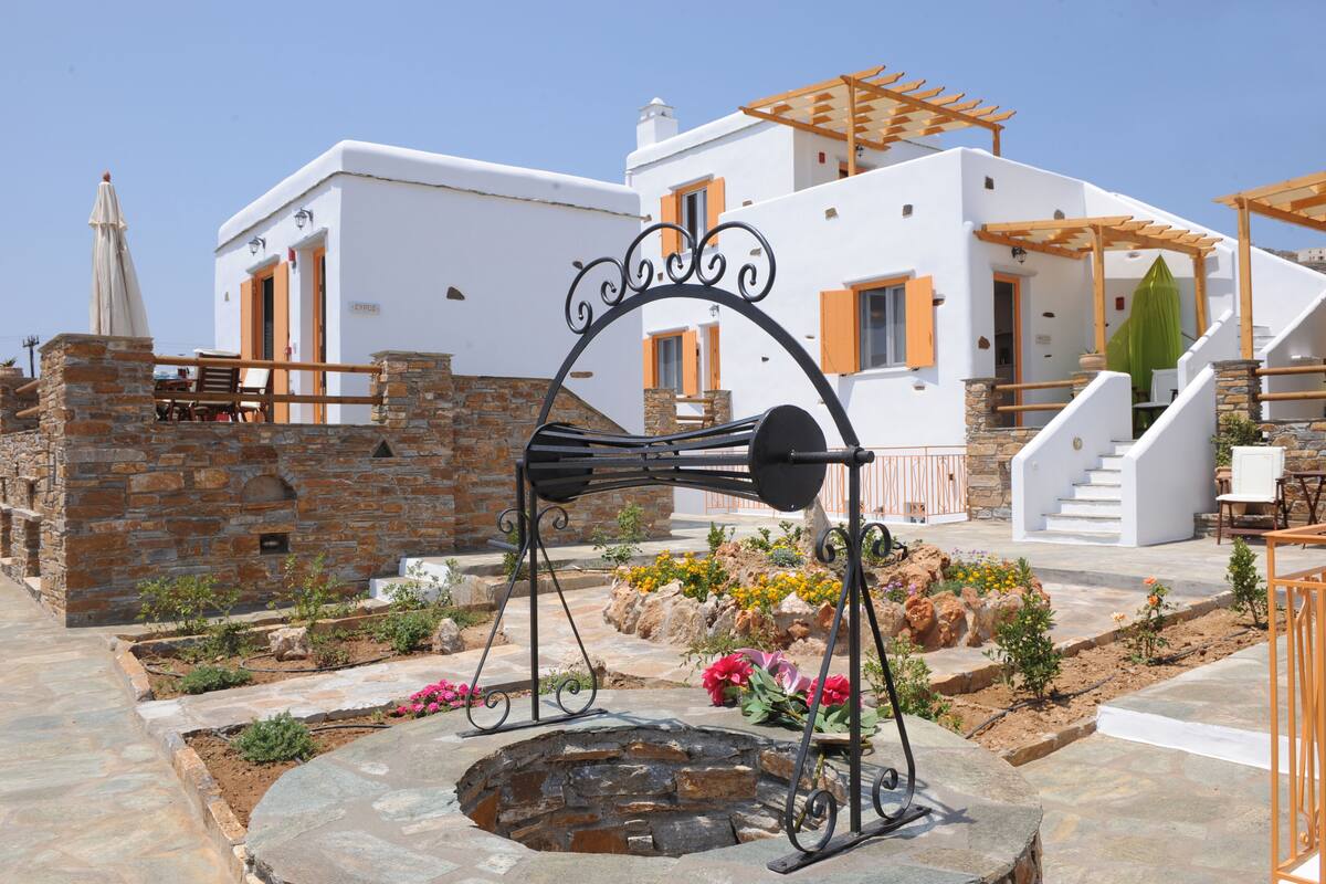 Un edificio blanco con muros de piedra, un pozo de piedra y una pérgola de madera.