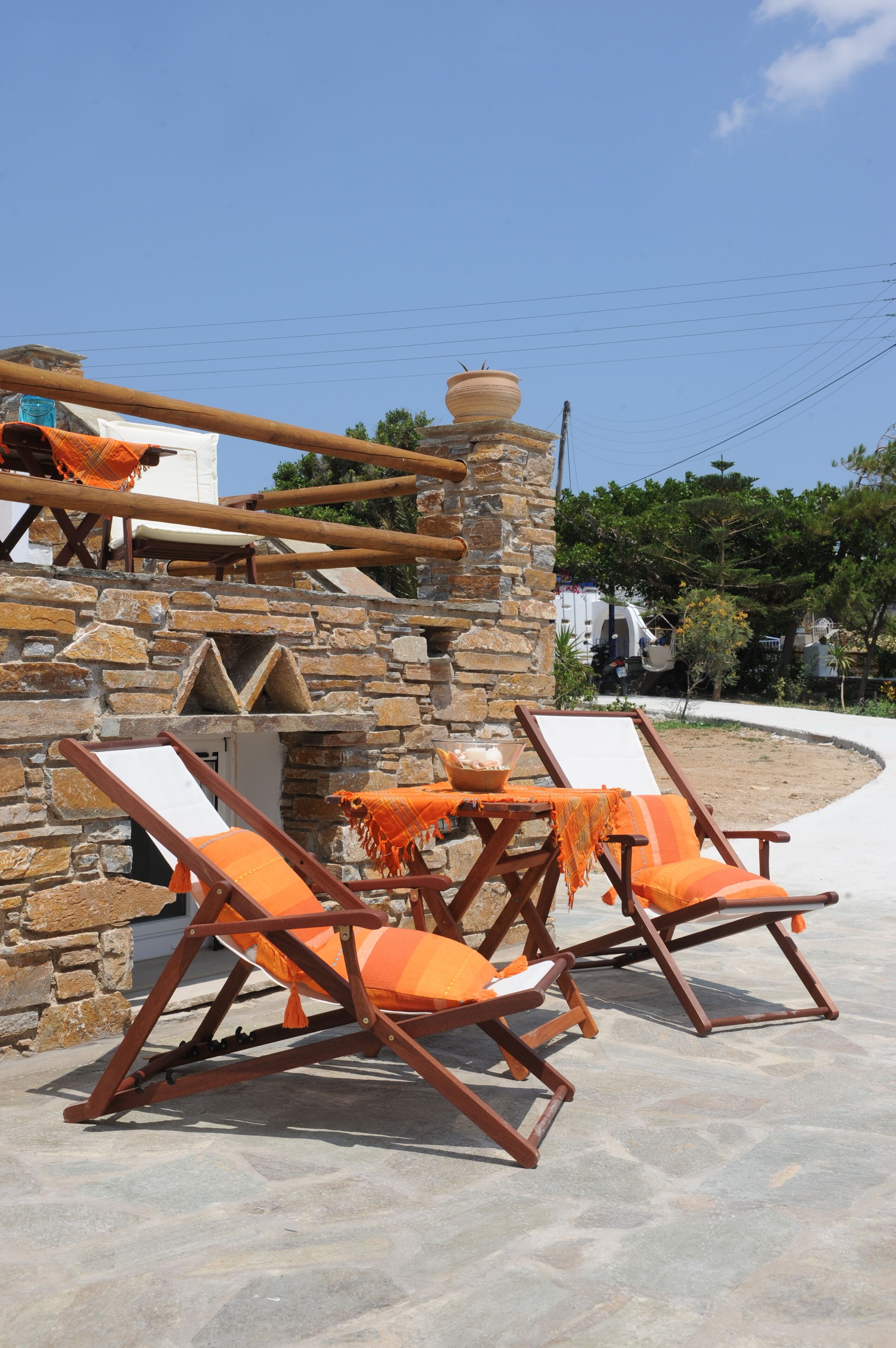 A stone building with a stone staircase, wooden deck chairs with orange cushions, and a clear blue sky.