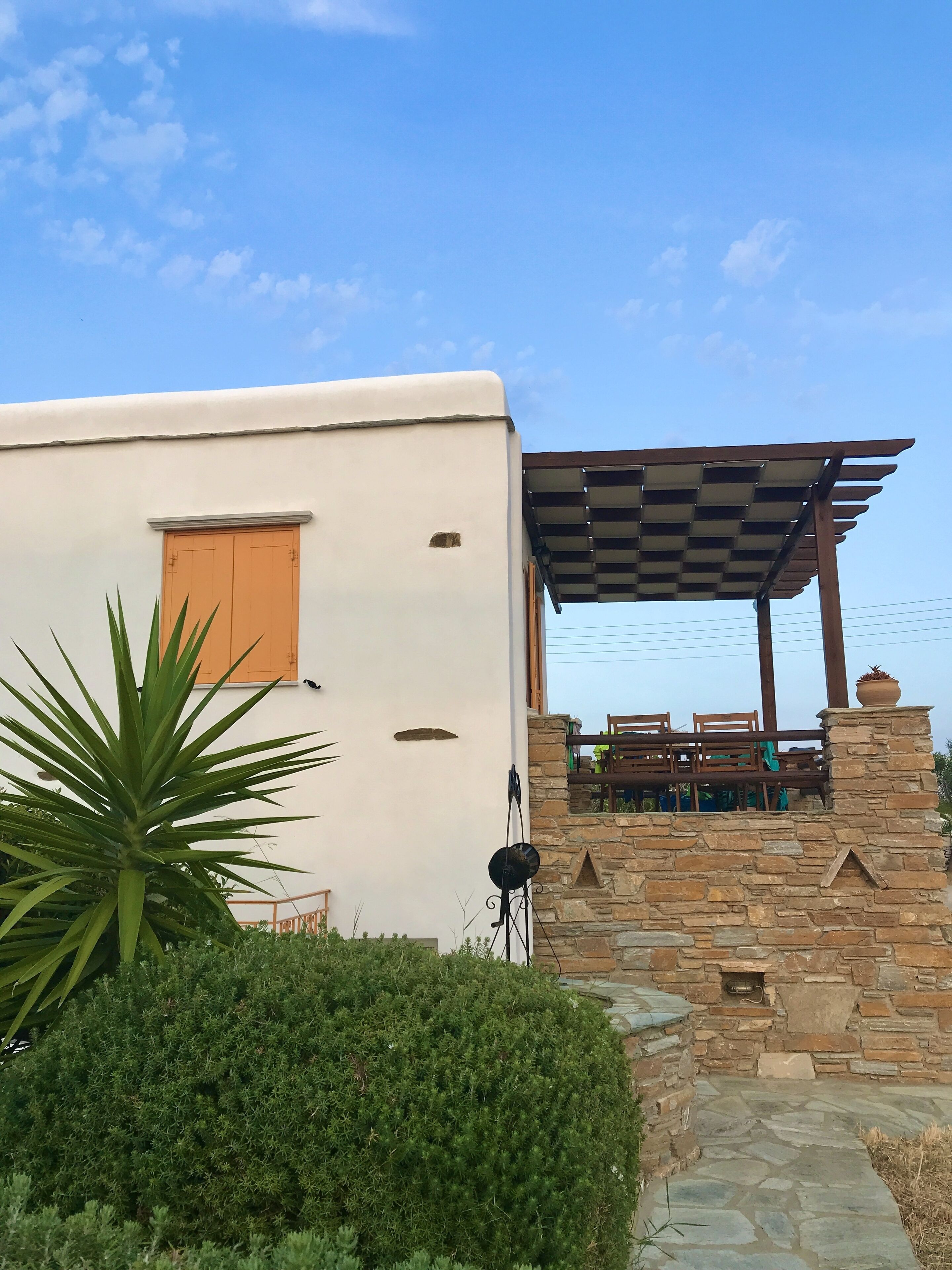 Un bâtiment à l’extérieur blanc, doté d’une pergola en bois et d’un mur en pierre.