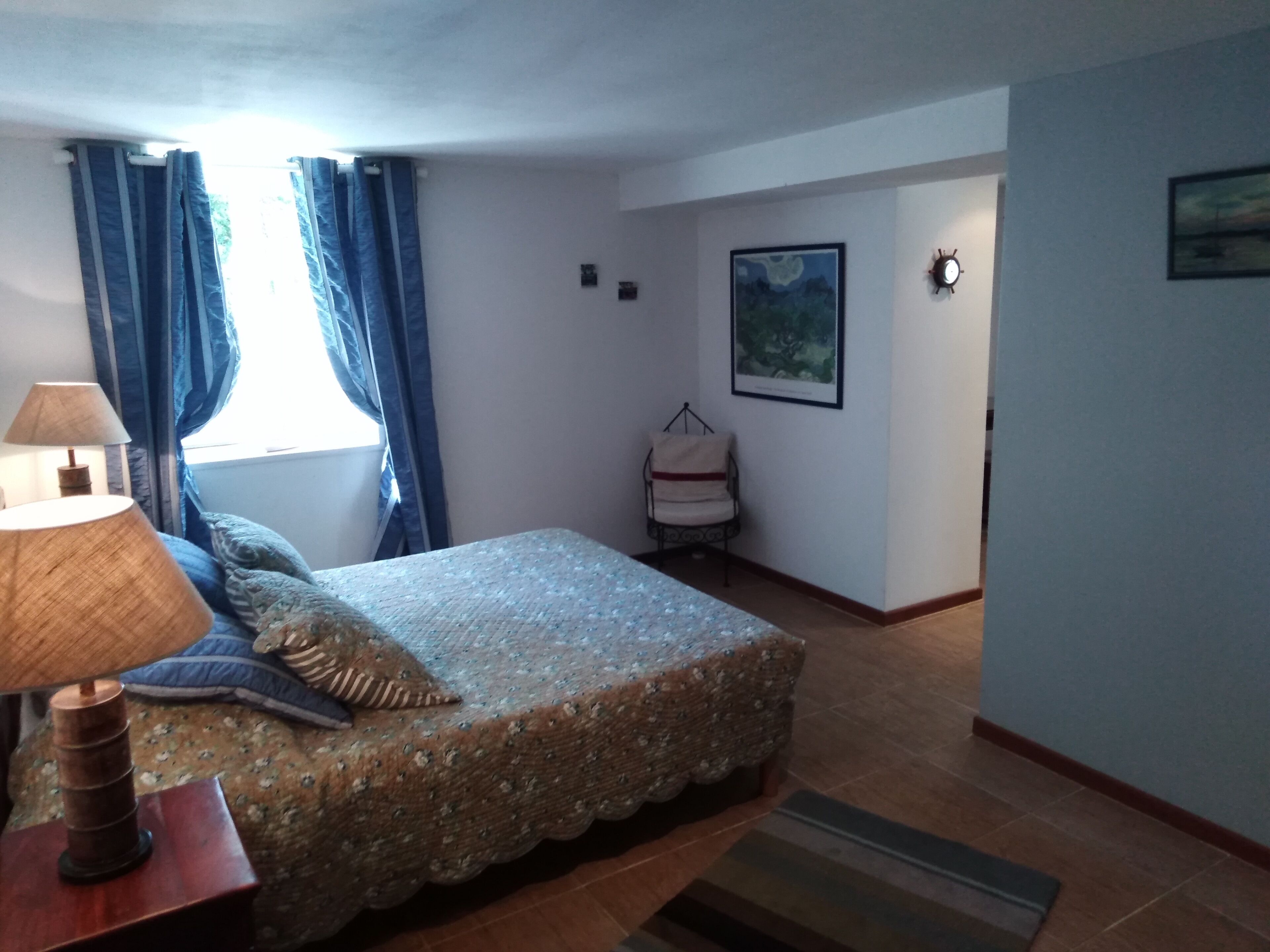 A bedroom with a bed, a lamp, a chair, and a painting on the wall.