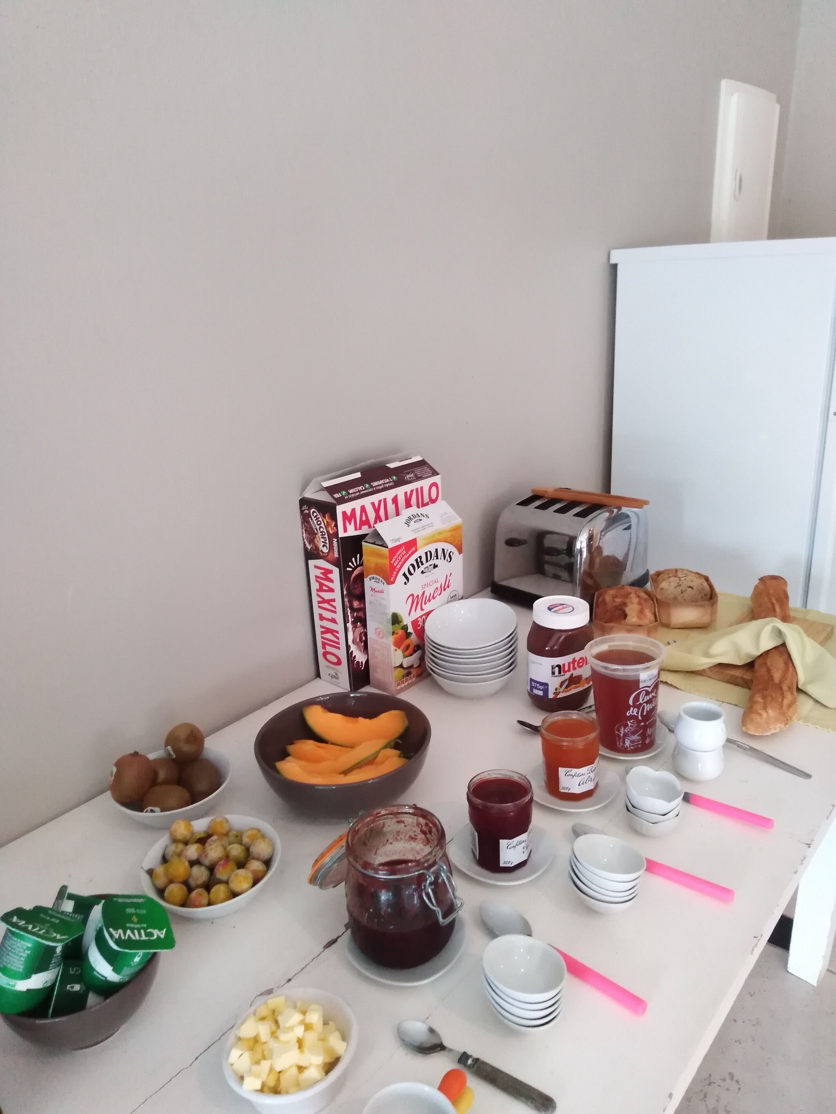 A breakfast table with various food items, including a carton of milk, a bowl of fruit, and a jar of jam.