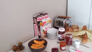 A breakfast table with various food items, including a carton of milk, a bowl of fruit, and a jar of jam.