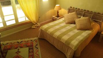 A bedroom with a bed, a nightstand, a lamp, a window with curtains, and a patterned rug.