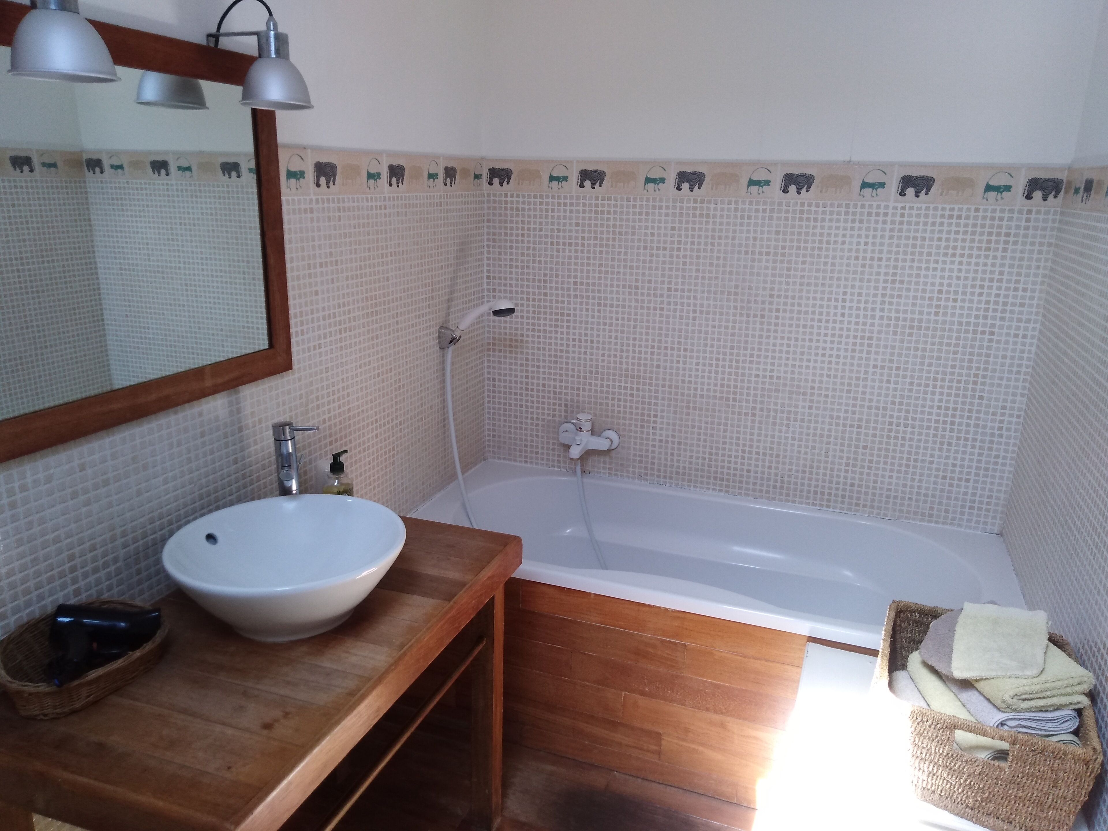 Een badkamer met een wit wastafel, houten opbergmeubel, een spiegel, een badkuip en een douche.