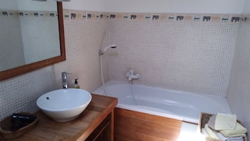 Een badkamer met een wit wastafel, houten opbergmeubel, een spiegel, een badkuip en een douche.