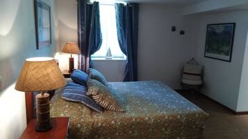 A bedroom with a bed, two lamps, a window with curtains, a chair, and a framed picture on the wall.