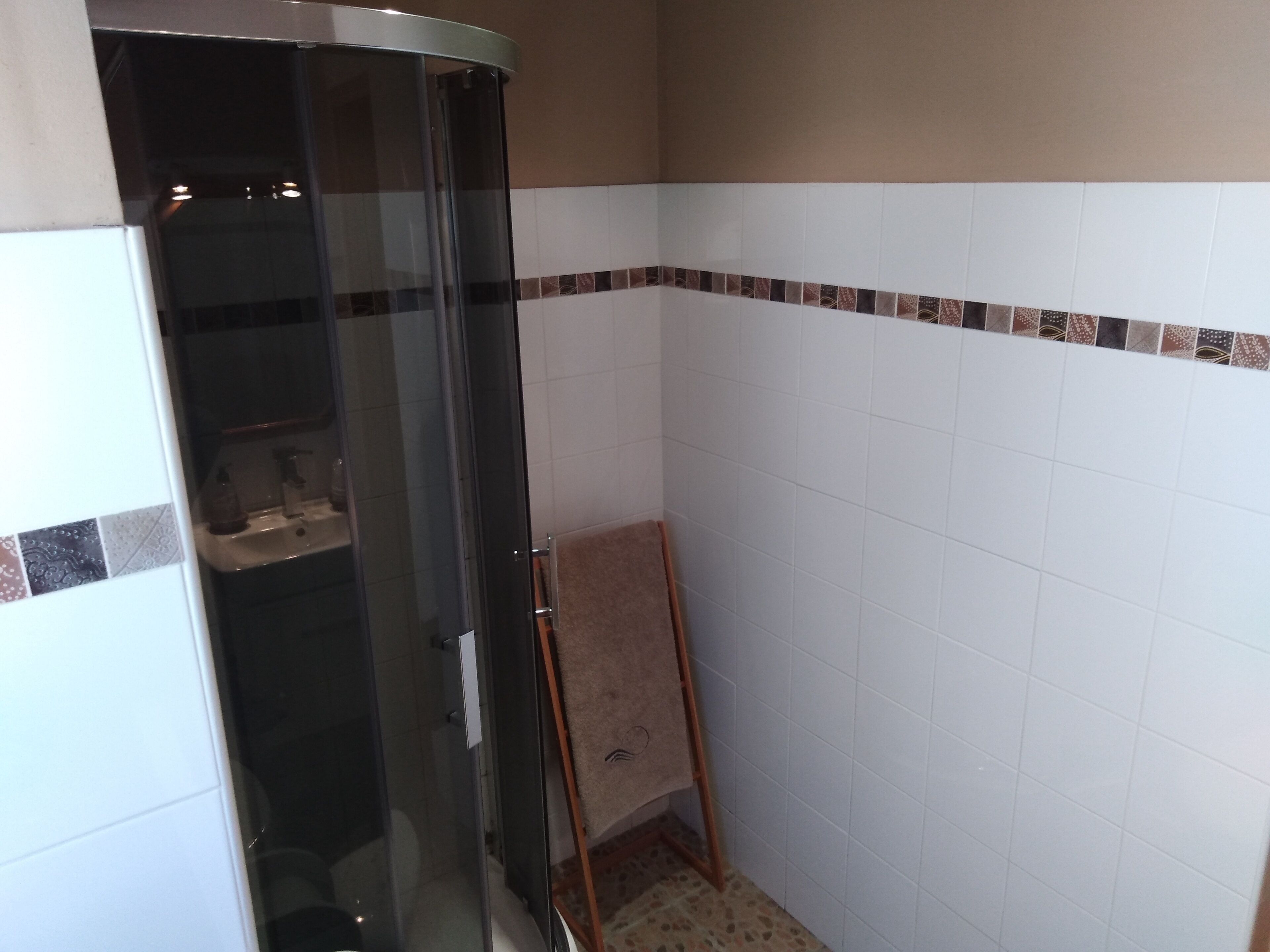 A bathroom with a glass shower enclosure, white tiled walls, and a patterned border.