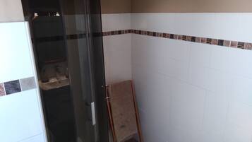 A bathroom with a glass shower enclosure, white tiled walls, and a patterned border.