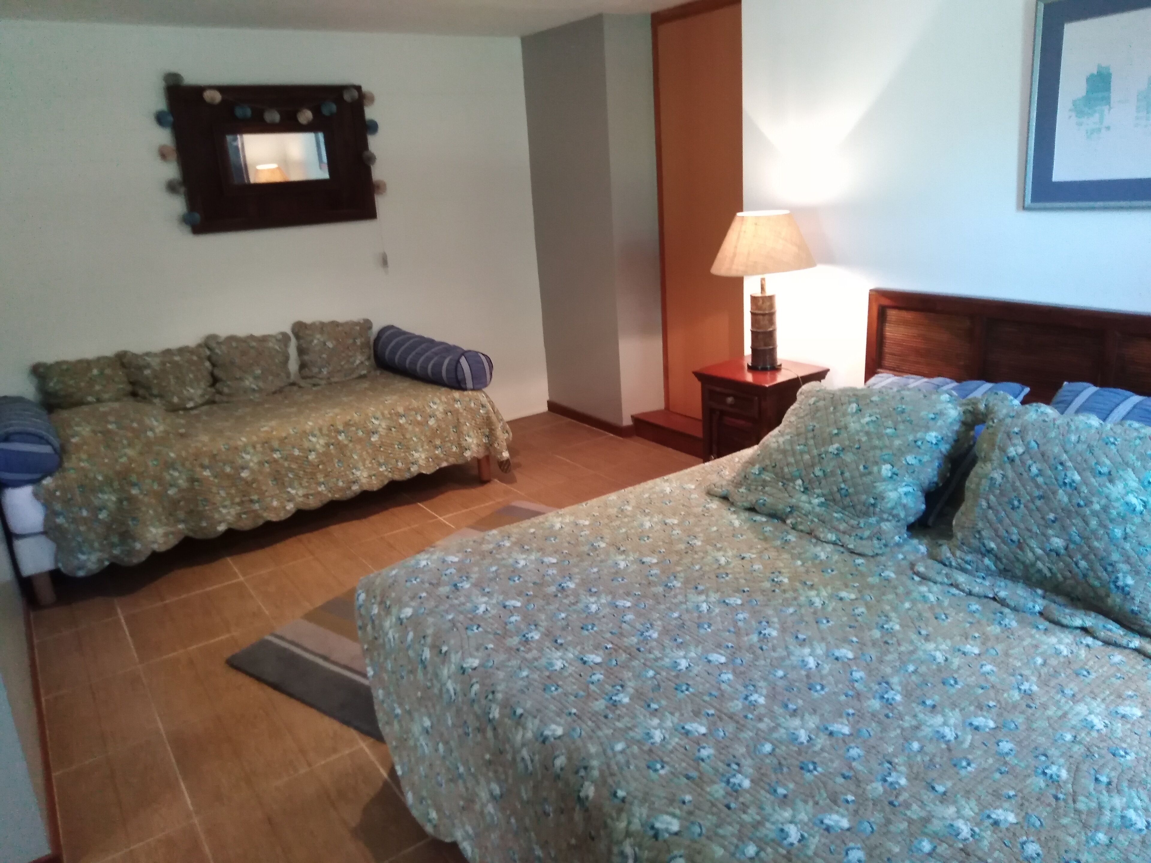 Een slaapkamer met twee bedden, een nachtkastje, een lamp en een spiegel aan de muur.