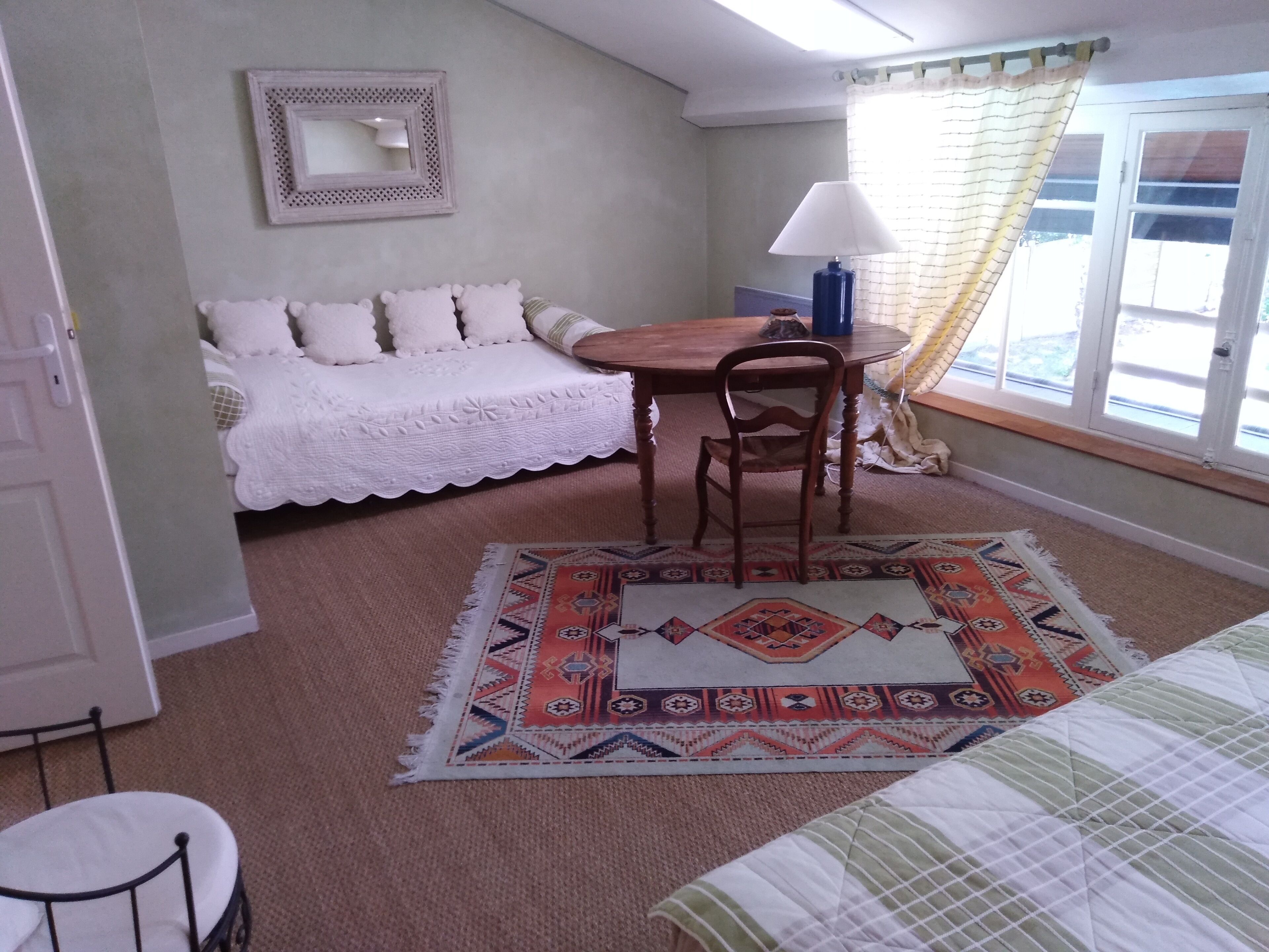 A small, cozy room with a white sofa, a wooden table, a blue lamp, and a patterned rug.