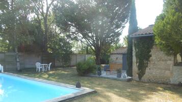 A backyard with a swimming pool, a stone building, and a wooden bench.