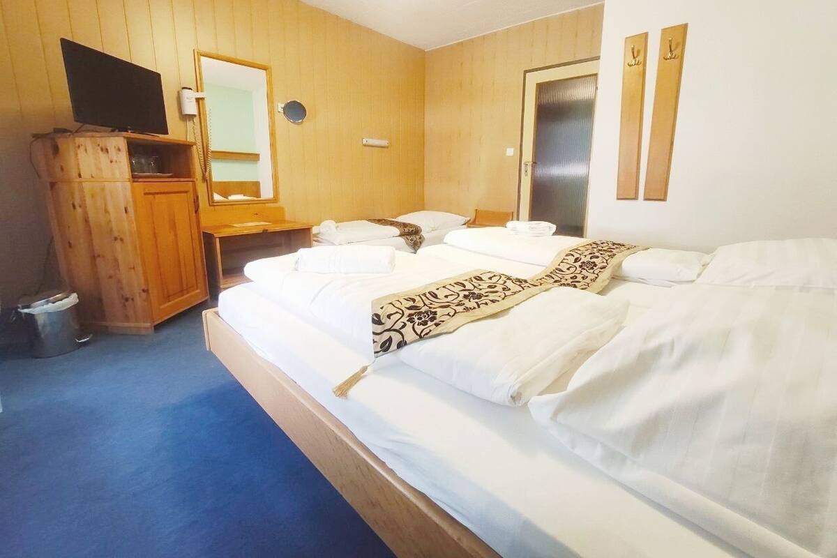 Ein Hotelzimmer mit Holzboden, einem Bett mit weißen Leinentüchern, einem Schrank aus Holz, einem Fernseher, einem Spiegel und einer Tür.