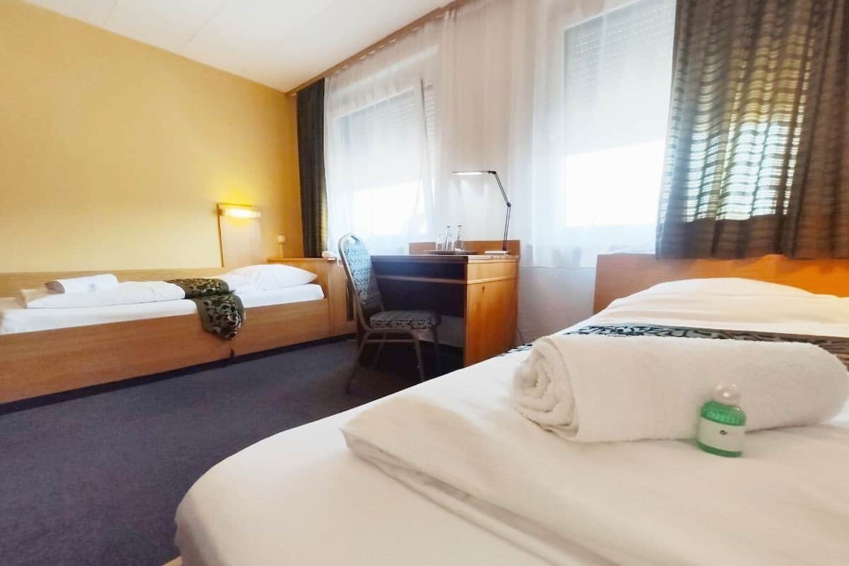 Ein Hotelzimmer mit zwei Betten, einem Schreibtisch, einem Stuhl und einer Lampe.