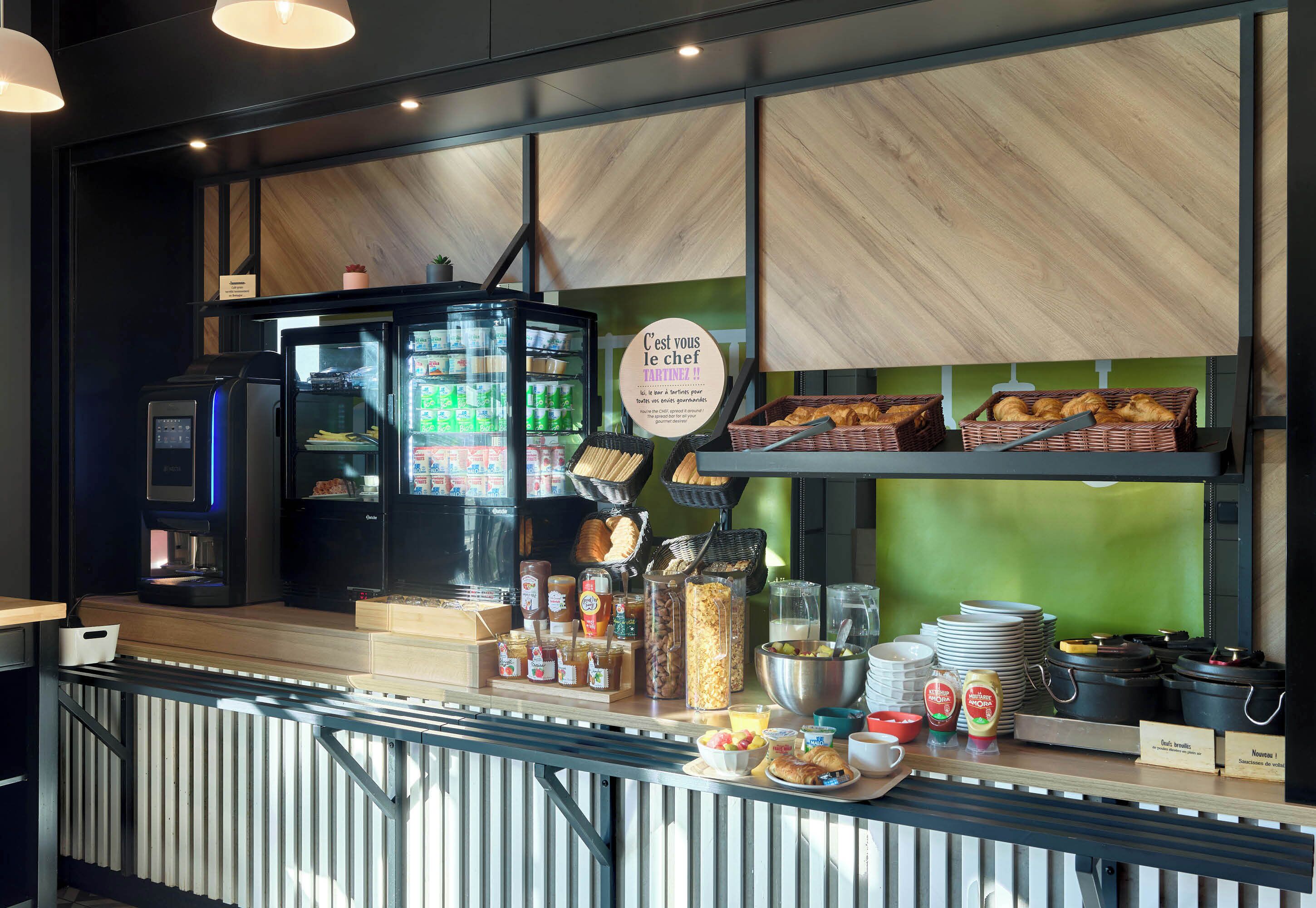 Un bar pour le petit-déjeuner équipé d’une machine à café, d’un réfrigérateur rempli de boissons et de divers aliments.