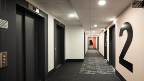A hallway with doors numbered 1 to 6, a carpet with text, and a corridor leading to a red-lit area. - B&B HOTEL Paris Meudon Vélizy (Meudon)