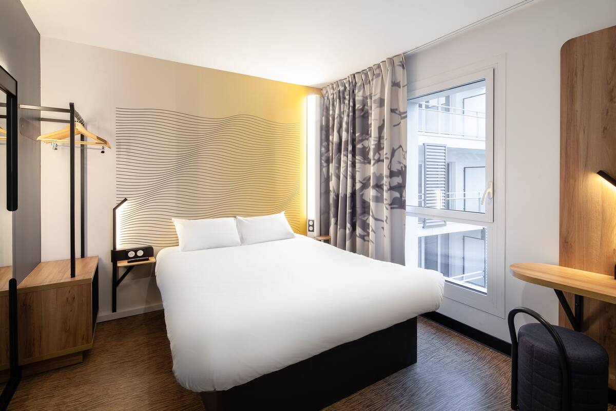 Una habitación de hotel moderna con una cama grande, mesitas de noche, un escritorio y vistas a la ciudad por la ventana.