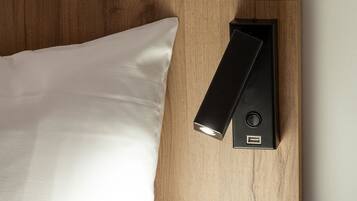 Una cama con un almohadón blanco y una mesita de noche negra con puerto USB.