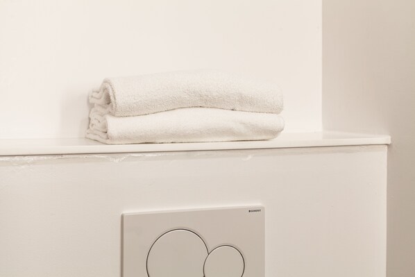 Una toalla blanca apilada sobre una superficie blanca, posiblemente un estante o mostrador, con el logotipo de GEBERIT visible en un objeto blanco debajo.