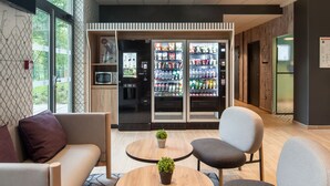 A modern lounge area with seating, a coffee machine, and a refrigerator stocked with beverages. - B&B HOTEL Paris Meudon Vélizy (Meudon)