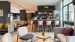 A modern lounge area with a bar, seating arrangements, and a view of the outdoors. - B&B HOTEL Paris Meudon Vélizy (Meudon)