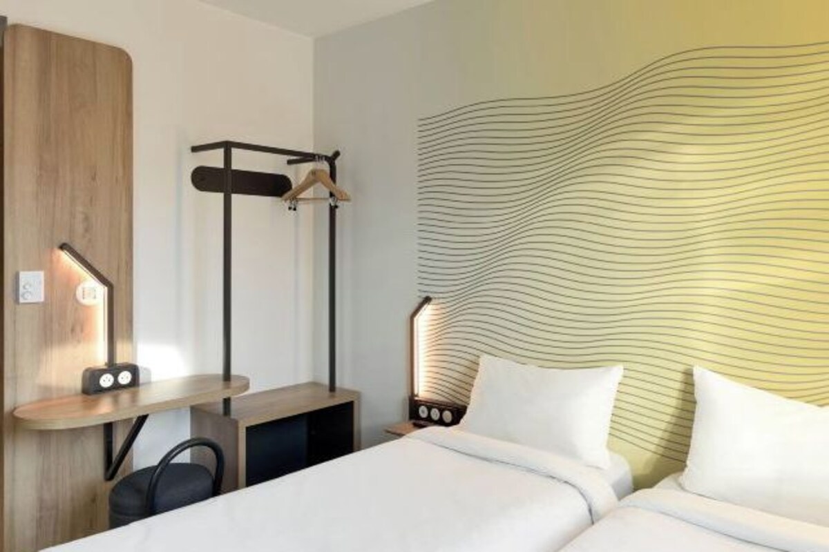 Een hotelkamer met een bed, nachtkastjes, een bureau, een stoel, een kapstok en een muur met een golvend patroon.