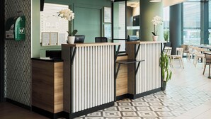 Un mostrador de recepción de diseño moderno, con una encimera de madera y un panel vertical. Tres lámparas colgantes iluminan el mostrador, y hay una planta en maceta sobre la encimera.