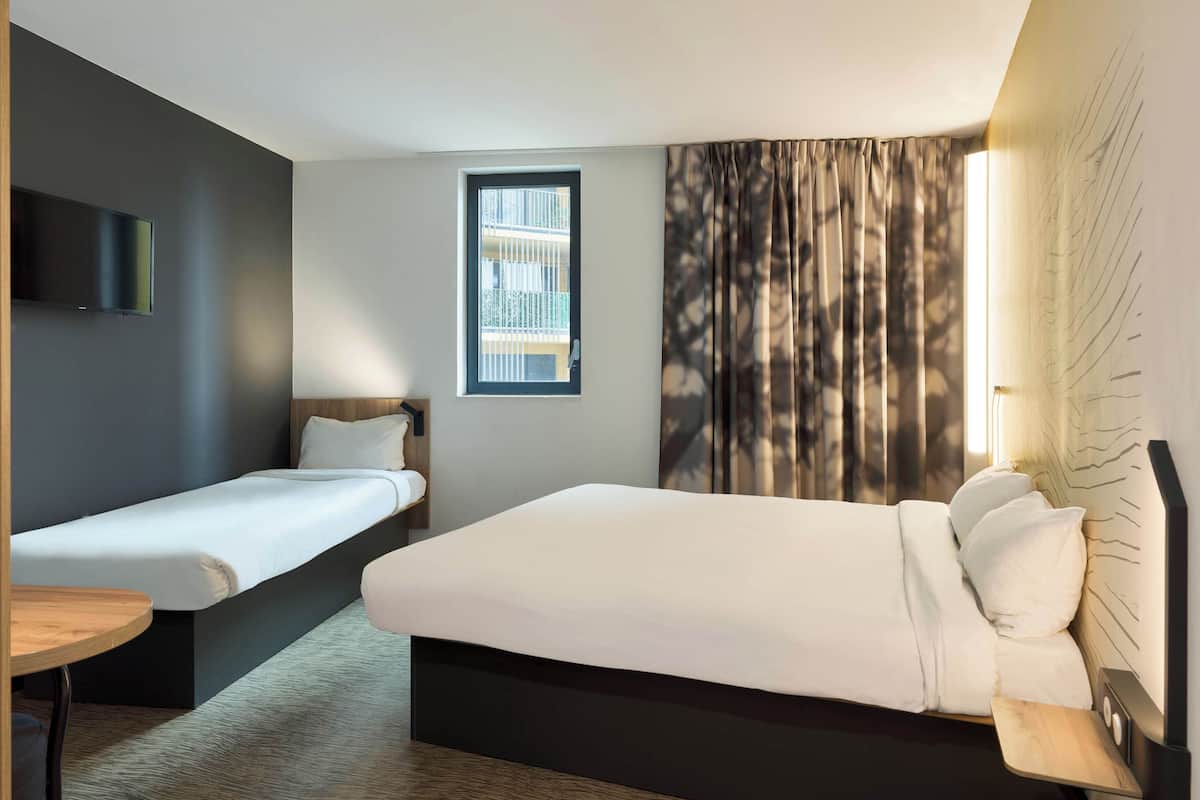 A hotel room with a large bed, a smaller bed, a TV, a window, and a curtain.